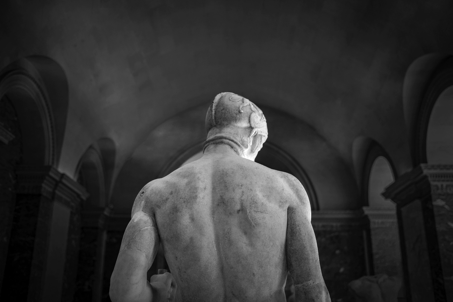 The muscular stone back of a man in statue. He looks down to the right.