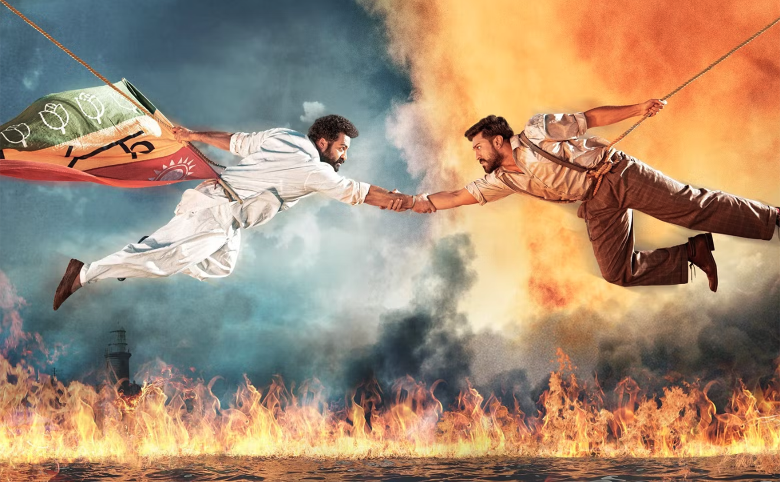  the two male stars of the movie rrr flying through the air while shaking hands with flames burning beneath them