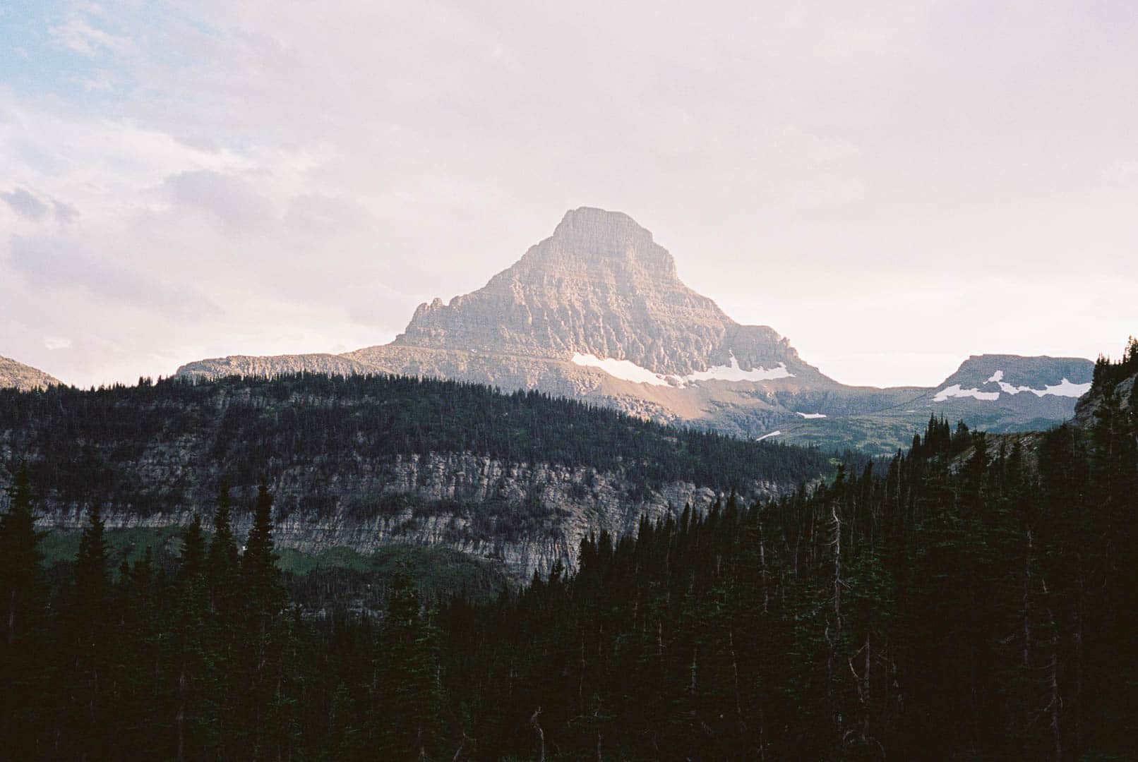 A rocky mountian peak sticking above treelined mountians