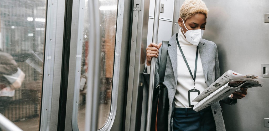 A women in office attire rides a subway car while wearing a medical mask to avoid getting sick from COVID-19.
