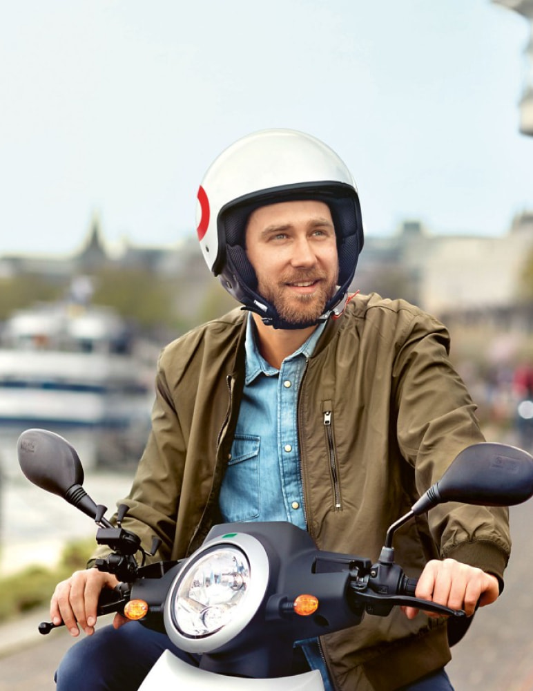 RheinEnergie customer hero image featuring a caucasian man in a helmet looking at something while sitting on his emoped.