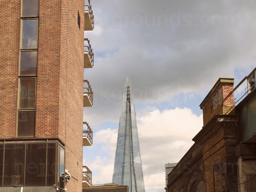 Urban London view of The Shard building featuring many reflective windows with red brick multi-story building in front Google Meet background