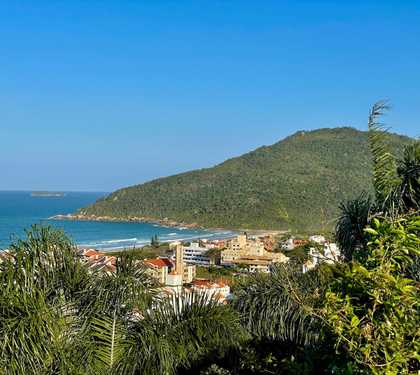 Vista de cima do mirante da praia brava onde se pode ver algumas residências o morro característico da praia e o mar azul.