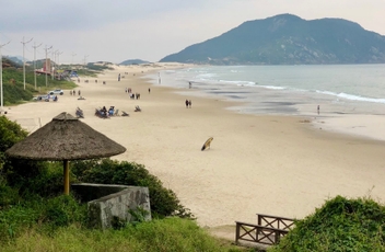 Vista da faixa de area da praia do Santinho, com mar a direita e montanha ao fundo