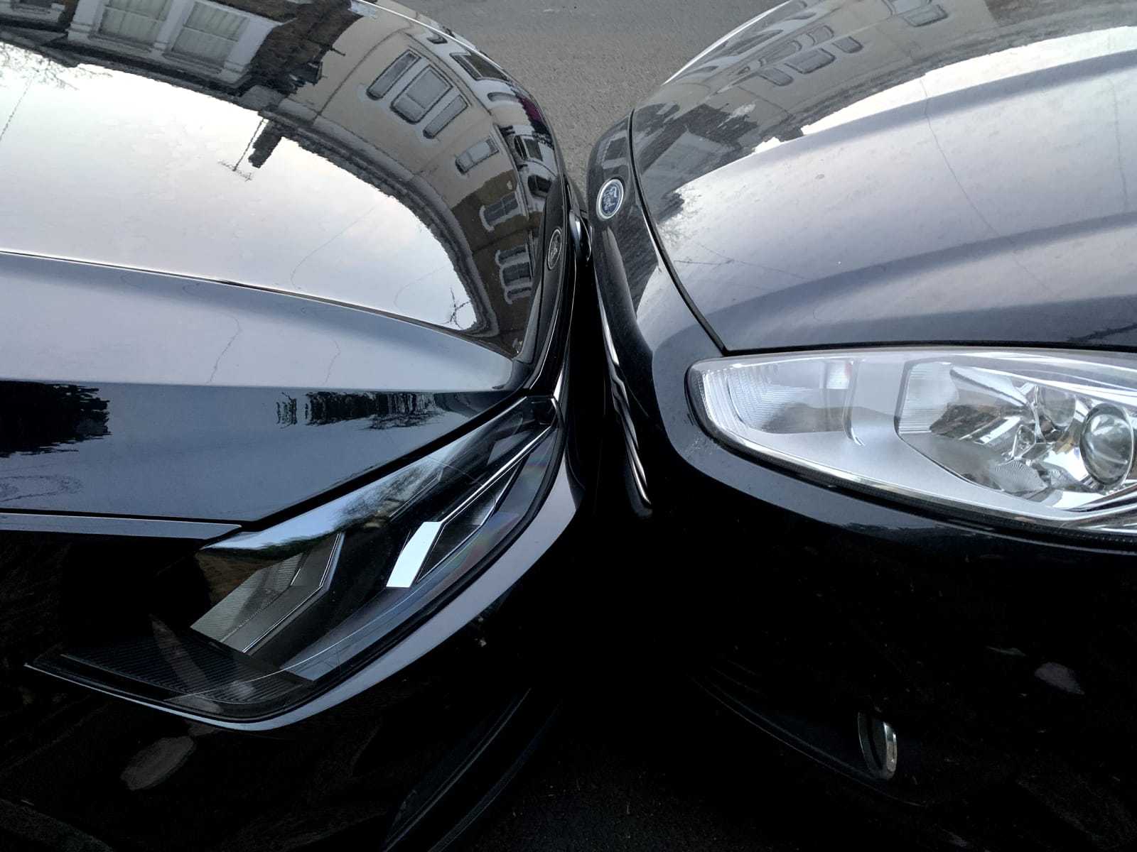 Two black cars parked so close together that their front bumpers are kissing