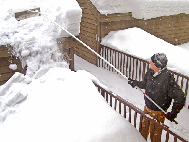 A man removing snow with a long brush in the winter