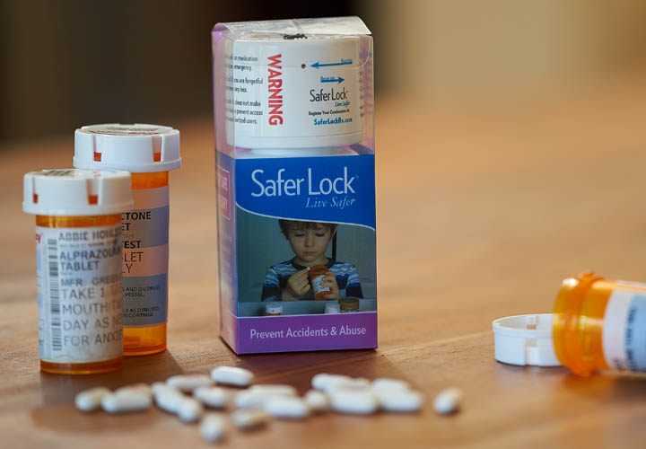 Photo of a Safer Lock bottle in packaging with pharmaceutical bottles and pills trewn around it.
