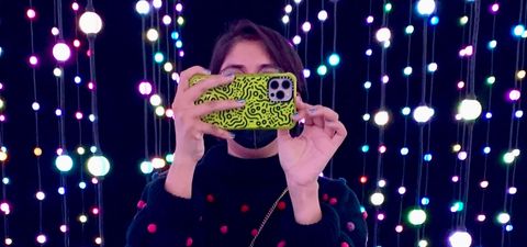 Sana at an art exhibit surrounded by lights holding up her phone.
