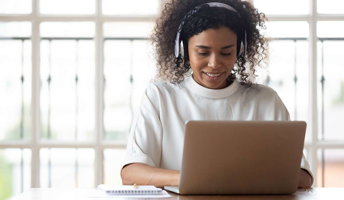 A woman wearing headphones taking training on her computer. Learn more about employee development in 2021.