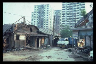 A crumbling kampong house captured in the process of demolition at River Valley Close while HDB flats stand tall in the background.