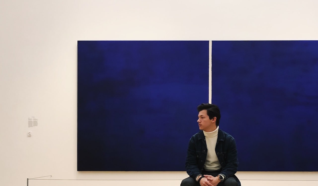 Didier Catz sitting in the Stedelijk Museum in Amsterdam, looking to his right, in front of a wide blue painting.