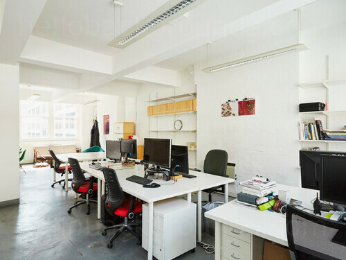 Contemporary  shared workspace containing white computer desks with black office chairs in front of large windows Skype background