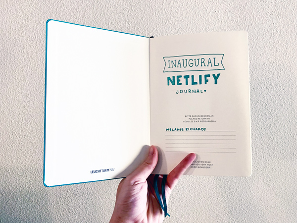 A teal journal opened to the first page, where I have written in teal pen 'Inaugural Netlify journal'