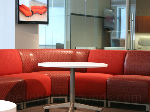 Sophisticated shared working area with red padded corner sofa around white table in front of wall mounted modern art Zoom background