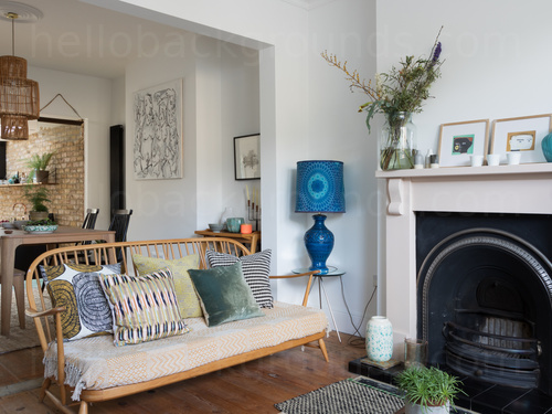 Light ornamental living room featuring wooden framed sofa with assorted patterned pillows and decorative fireplace Zoom background