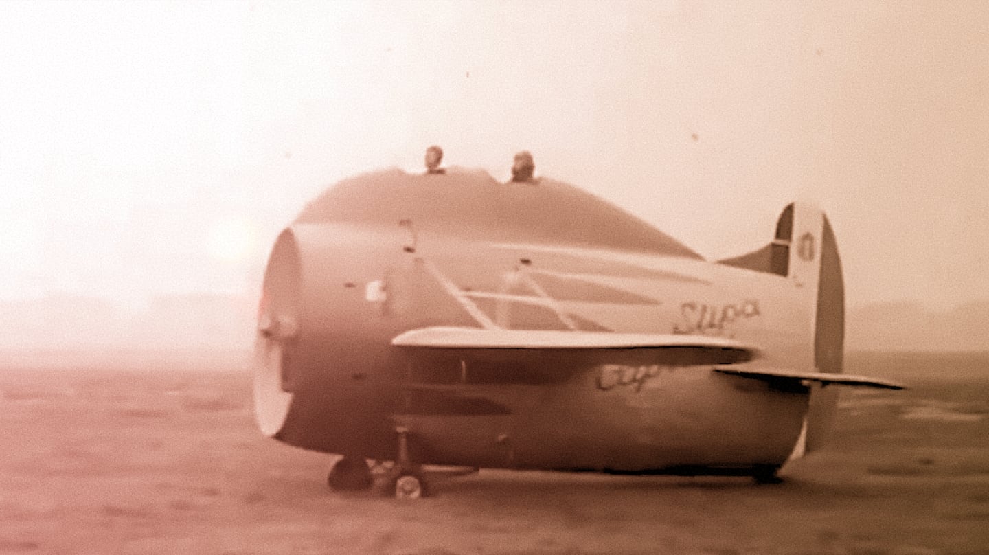 Vintage photograph of an airplane looking like a barrel. Two open cockpits in tandem are mounted in a hump on top of it.