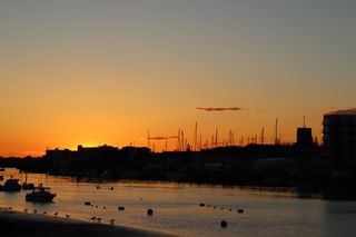 Sun setting behind the rooftops of Shoreham town. Silhouettes of small boats and birds line the river Adur below.