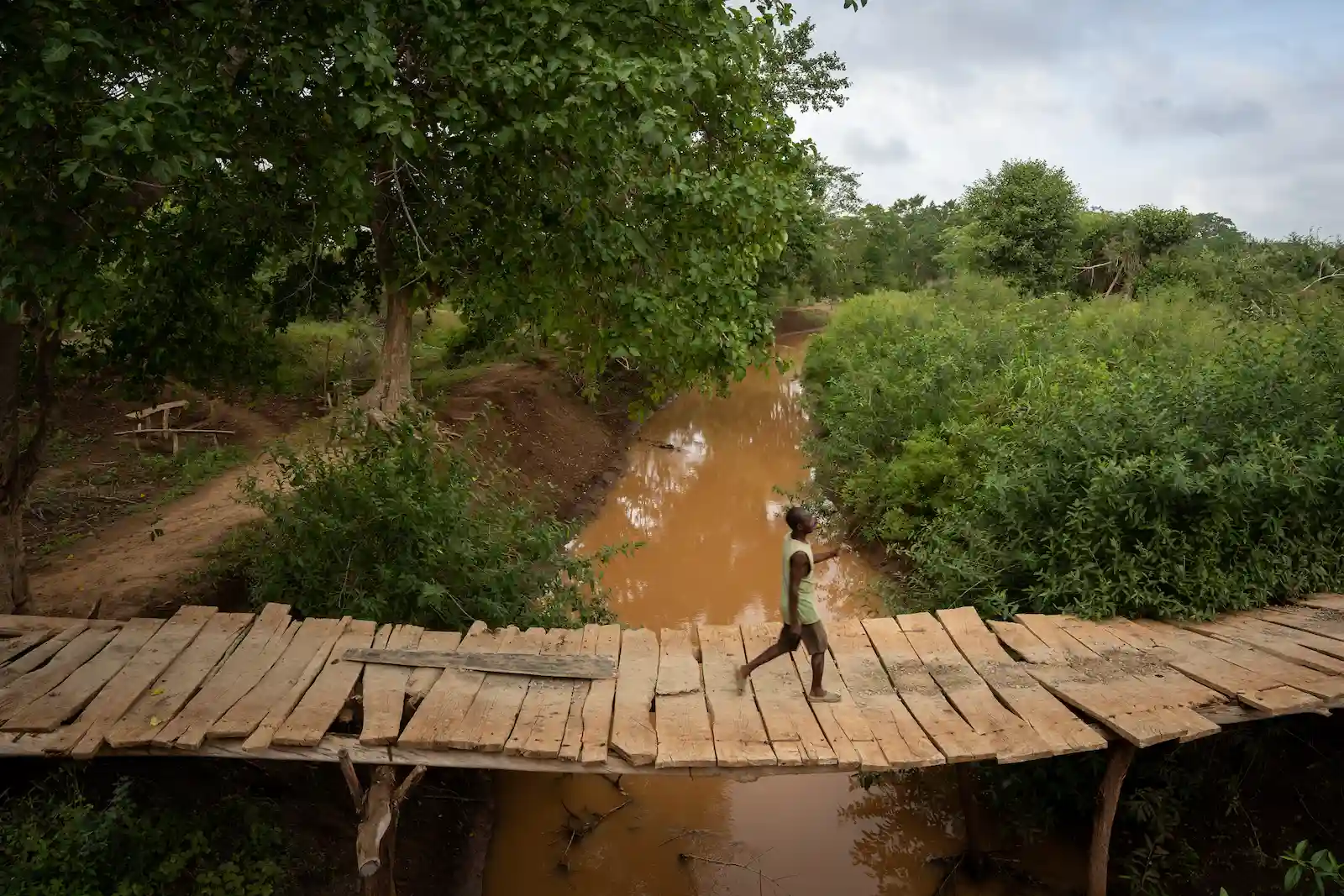 A man uses a small bridge to cross a river in Kenya