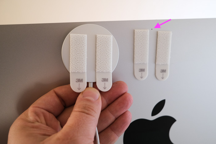 An Apple Studio Display with a MagSafe charger attached to the back using 3M Command Strips. The Command Strips avoid covering the Studio Display's microphone. The microphone is highlighted with a pink arrow