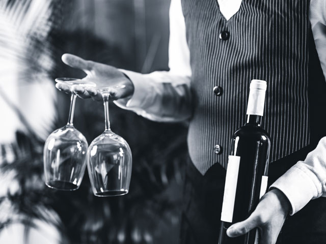 A Sommelier holding a wine bottle and two wine glasses with no way to open the bottle