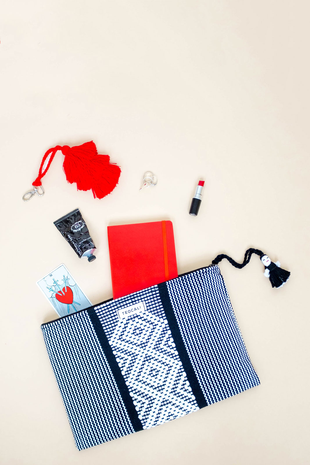 Flatlay of woven bag with lipstick, tarot card, etc, spilling out.