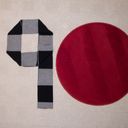 Laid out on a beige rug, a black and grey folded scarf and a round red mat form the digits nine and zero.