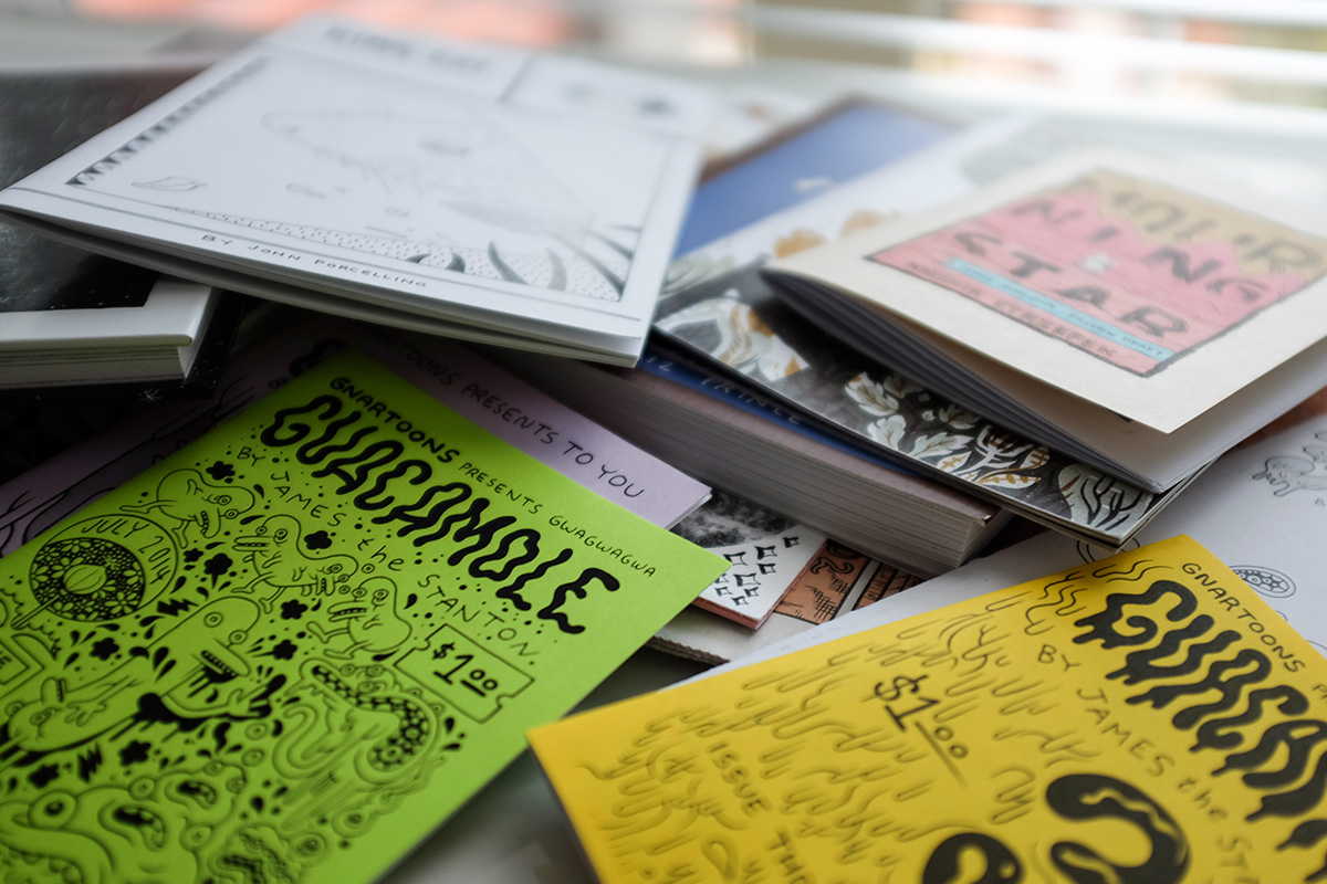 A pile of comics in various styles layered on top of a desk