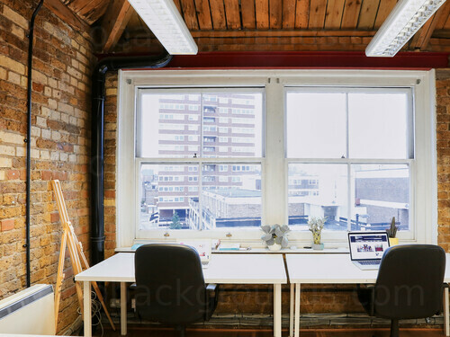 Well lit private office with exposed brick decor and city views featuring double desk with black office chairs Zoom background