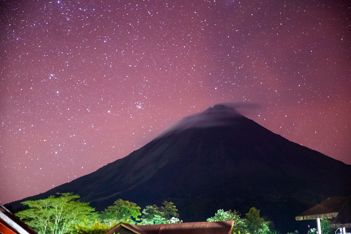 Stars glitter a purple sky above Arenal Volcano at night.
