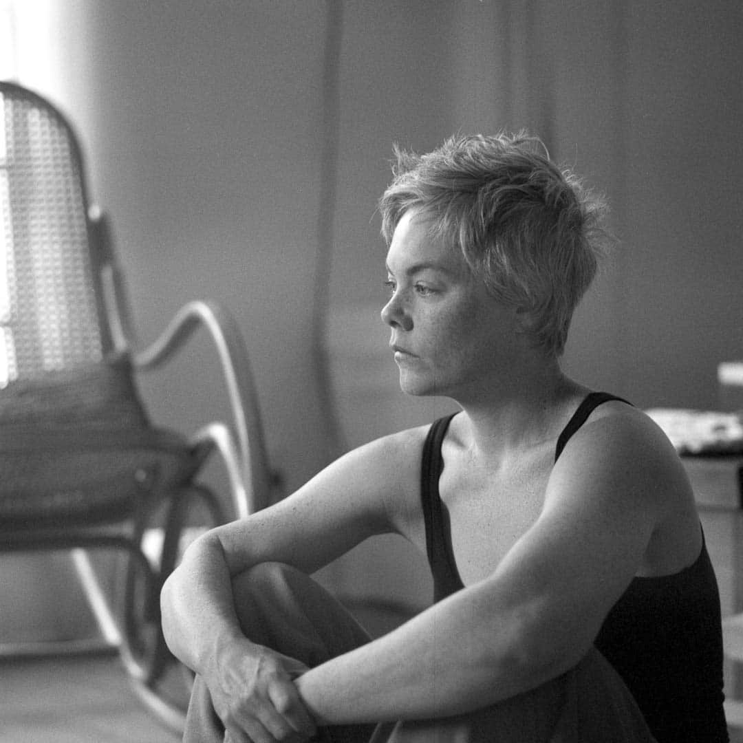 A woman sitting on the floor in a room filled with natural light looking off into the distance