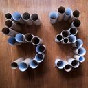 Looking down upon a collection of cardboard tubes sitting upright on the floor. They are clustered into the shape of the digits five and three.