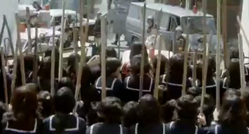 A screenshot of Japanese school girls carrying shinais clashing with a police barricade. From the film 'Terrifying Girls High School: Lynch Law Classroom'.