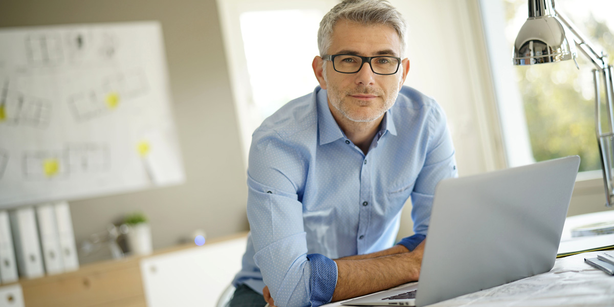 A UI designer sitting at his desk with a laptop A User Interface Designer smiling slightly, sitting in front of his laptop