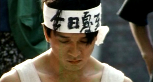 A close-up screenshot from the Chinese film 'Frozen' showing an artist wearing a white bandana with Chinese characters written on it.