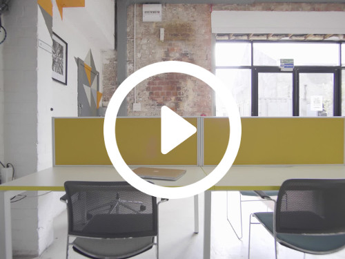 Simple shared workspace featuring exposed red brick walls with basic yellow and white desks next to black office chairs Google Meet background