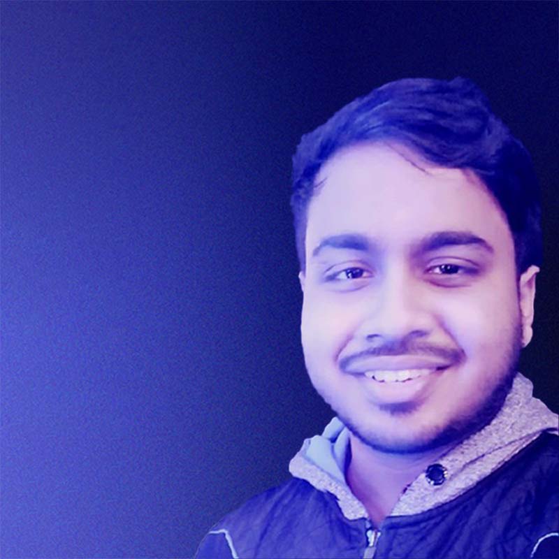 subham kundu, a man with short dark-brown hair and beard who’s wearing a hoodie, smiles while standing in front of a purple-colored background