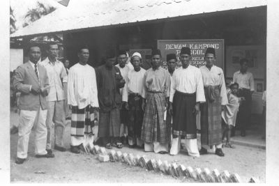A black and white group photo of ten Malay men, likely community leaders, standing outside the Punggol Malay School during its official opening. Most are dressed in baju Melayu (traditional Malay costume) and songkoks (traditional Malay headgear).