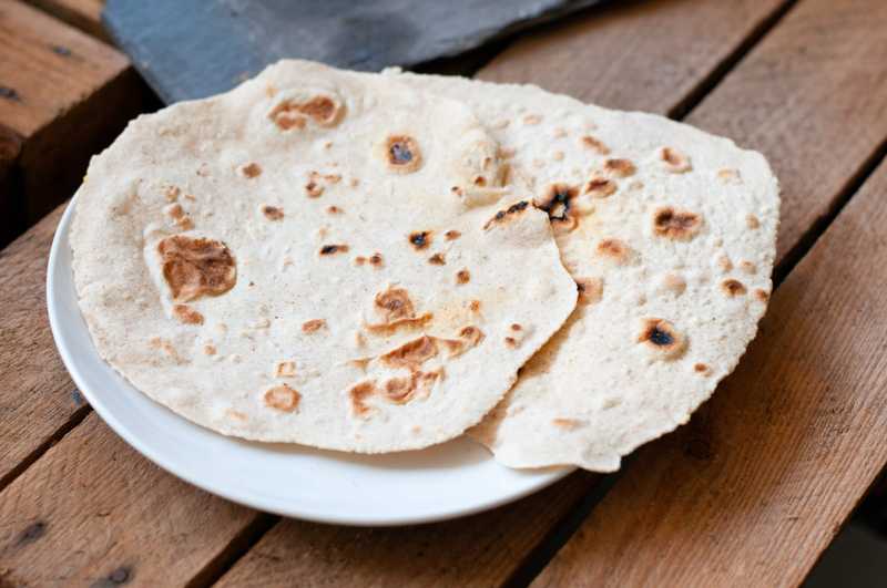 Une pile de tortillas sur une assiette. Les tortillas sont circulaires, fines et plates. Elles sont pour la plupart de couleur pâle avec des bulles d'air brunies.