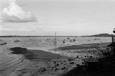 A black and white photo of the sea, with sand banks of Punggol beach in the foreground. Around 18 pleasure boats are on the water.