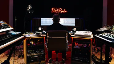 A shot of Zahl from behind, sat in the middle of his studio, surrounded by synths and other audio equipment