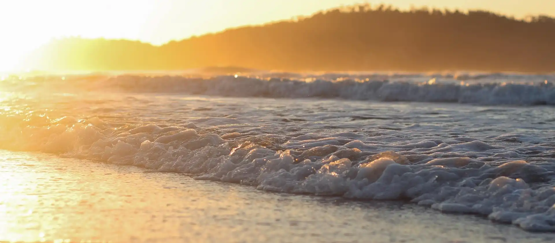 Destaque no mar com espumas de ondas e por do sol alaranjado refletindo na água