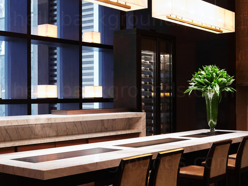 Sophisticated restaurant interior featuring long white marble table with wooden seating next to windows Skype background