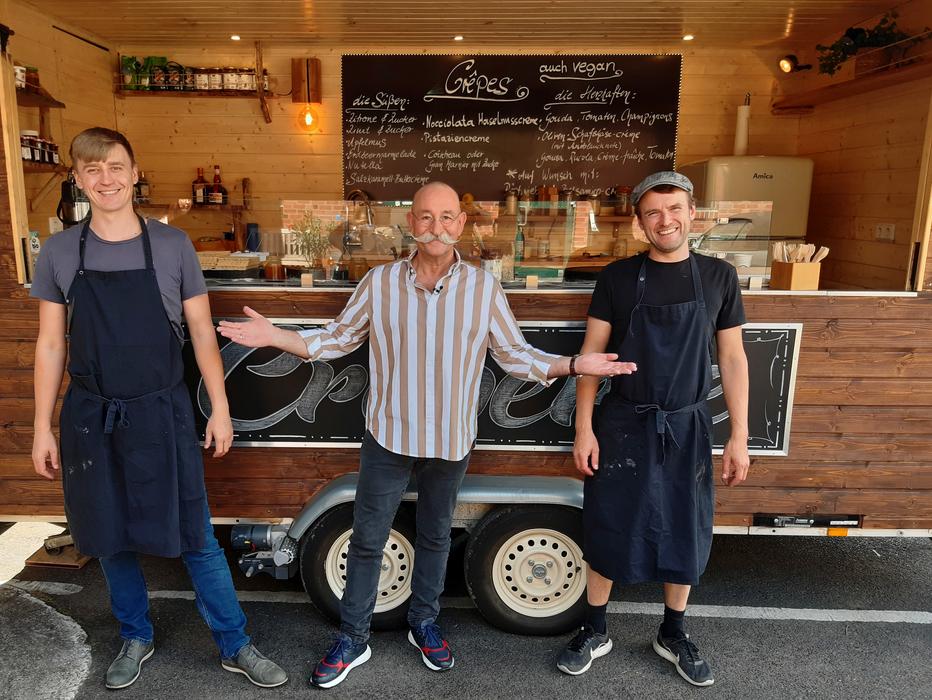 Horst Lichter steht mit zwei Catering Mitarbeitern lächelnd vor dem Crepe Foodtruck nach einer Filmklappe