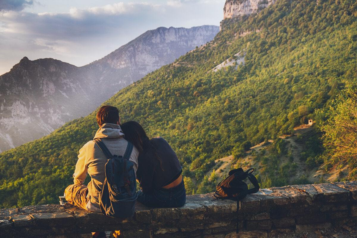 A couple of travelers sitting together in front of a mountain.