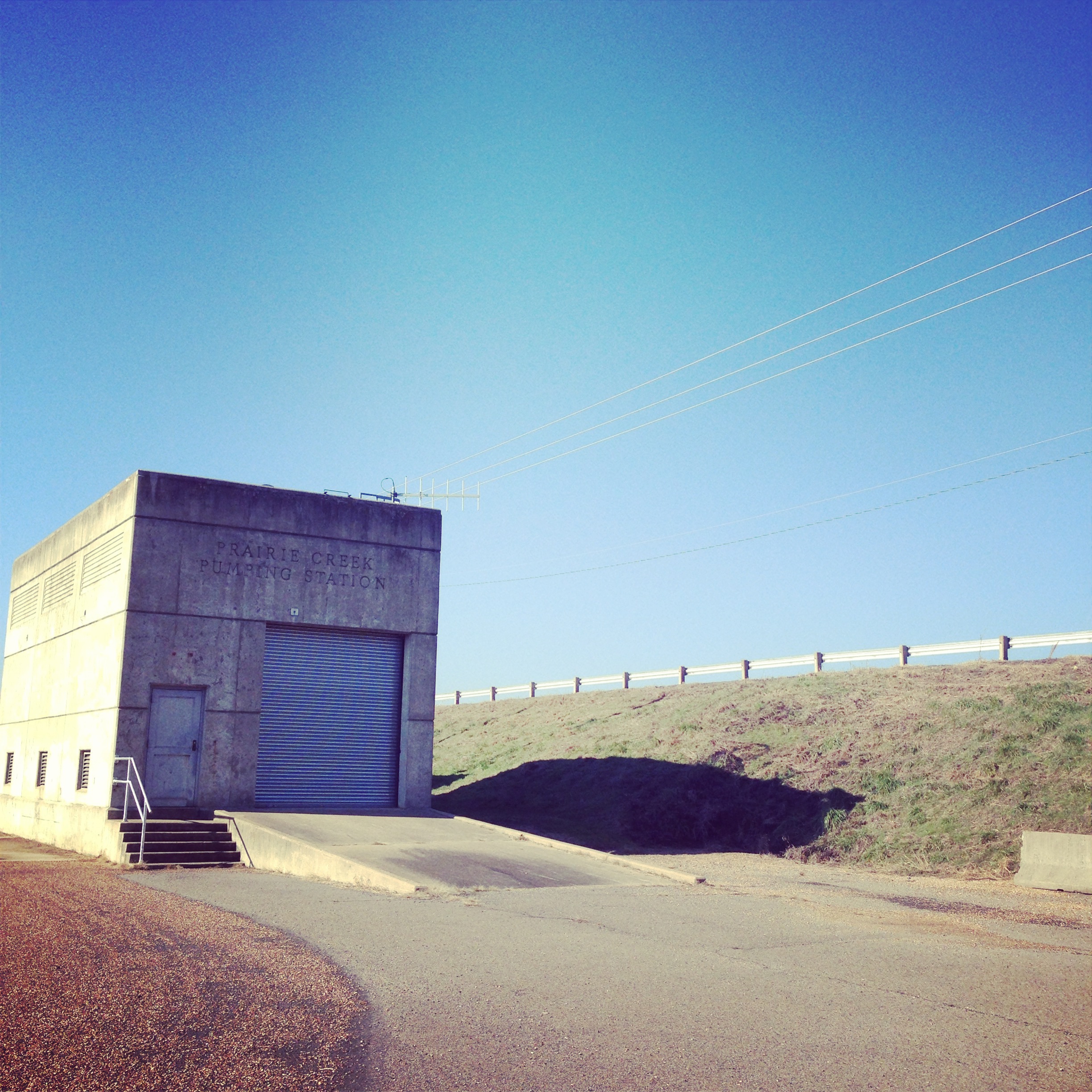 A public facilities building at Bona Dea Trail in Russellville, Arkansas: a simple concrete warehouse. The garage door is approached by a simple concrete ramp.