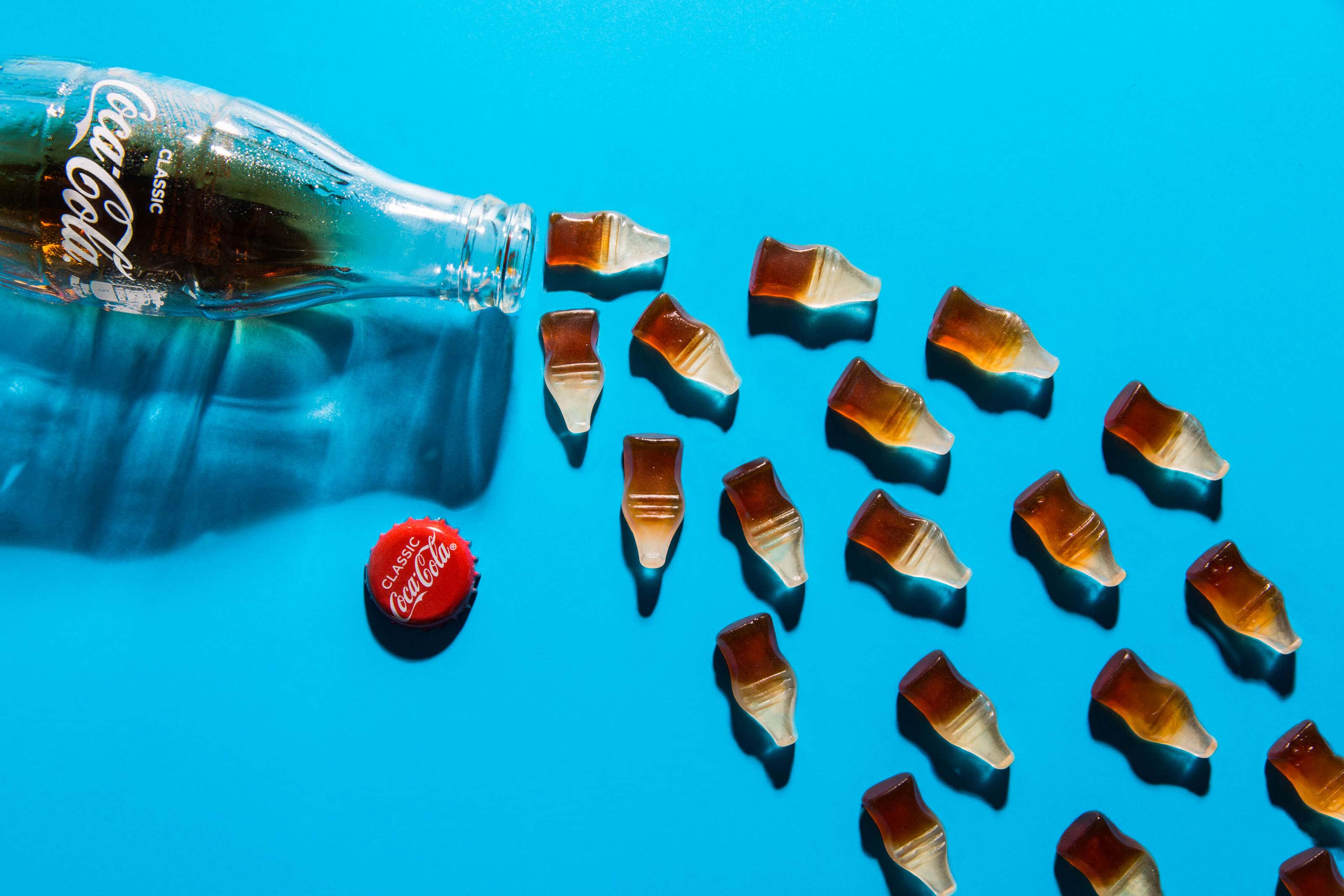 Coca-Cola bottle with coke sweets Pouring out on blue background pop art style