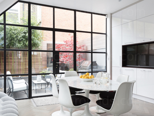 Large dining area featuring floor to ceiling windows and table and white chairs with black upholstery Microsoft Teams background