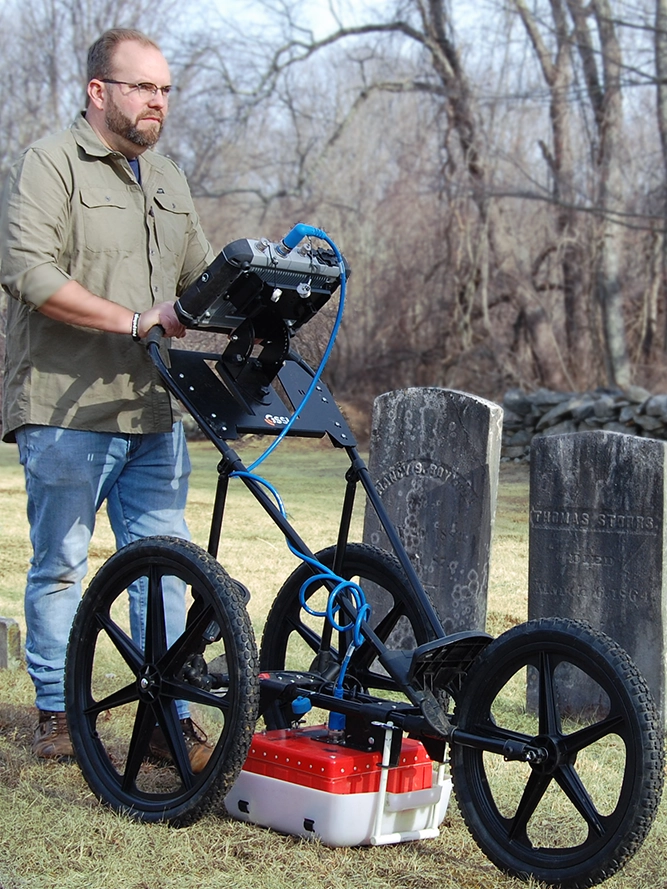 Man using a ground penetrating radar machine in a cemetery.