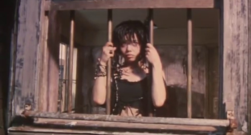 A screenshot of a gothic woman behind window bar cells looking outside at the sun. From the film 'Picnic'.