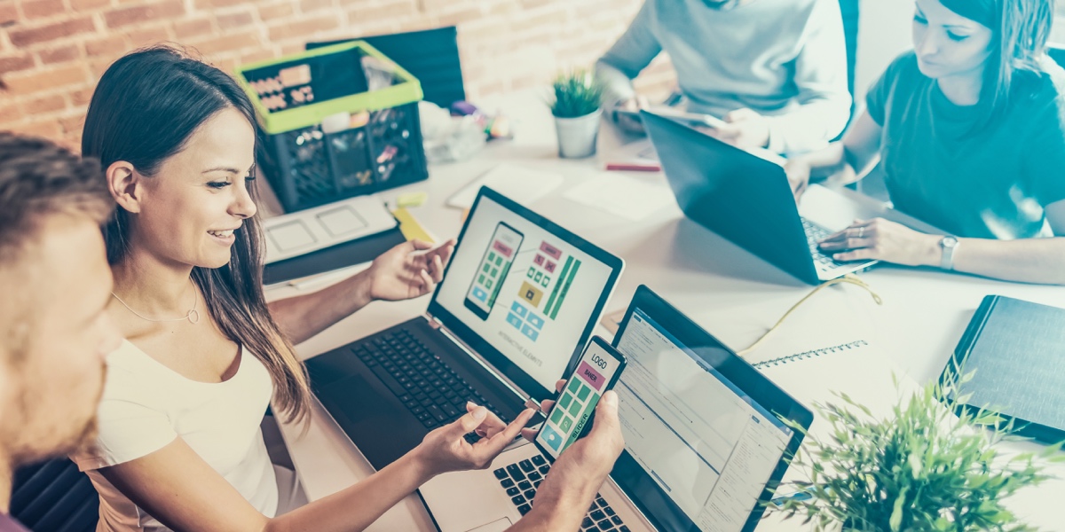 What Is User-Centered Design? Four designers working at a desk in an open office with laptops and other devices